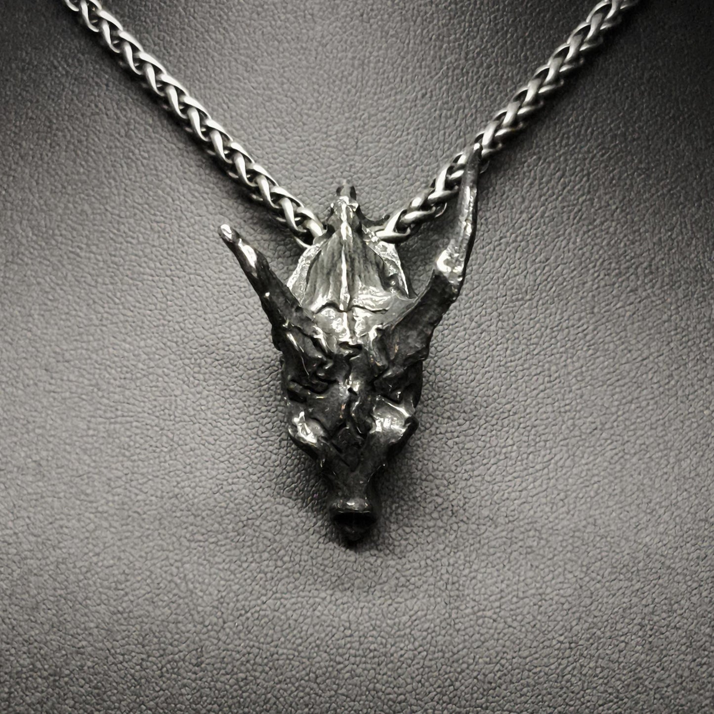 Metallic dragon head pendant on a chain against a dark background
