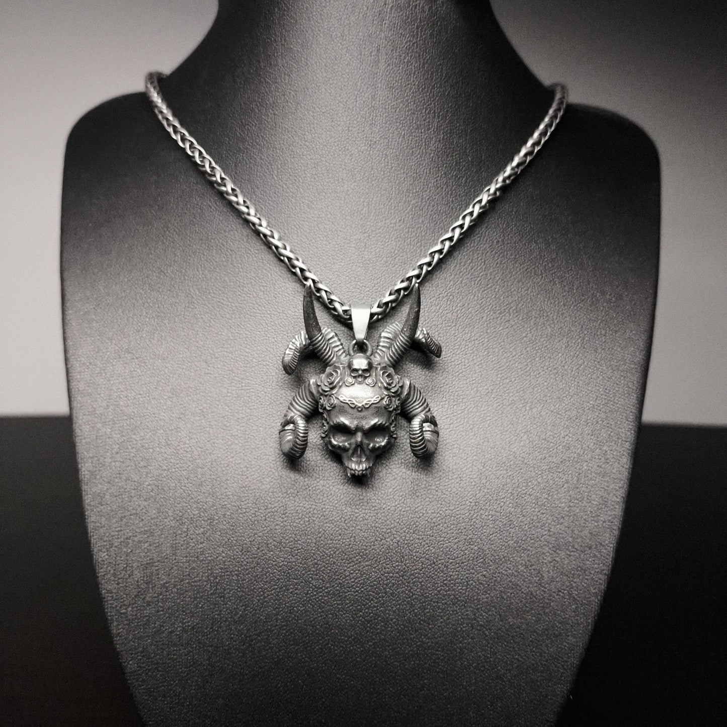 Silver necklace with a detailed pendant on a black mannequin bust.