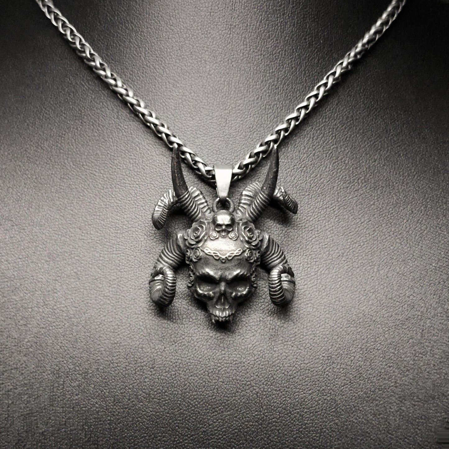 A stainless steel pendant featuring a tribal skull design, displayed on a mannequin neck.