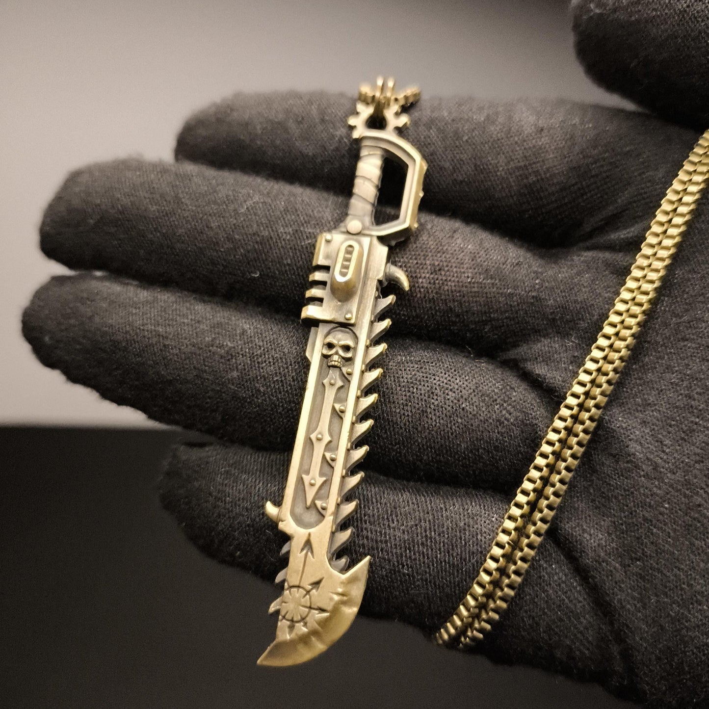 Gold sword-shaped keychain held in a black gloved hand against a dark background