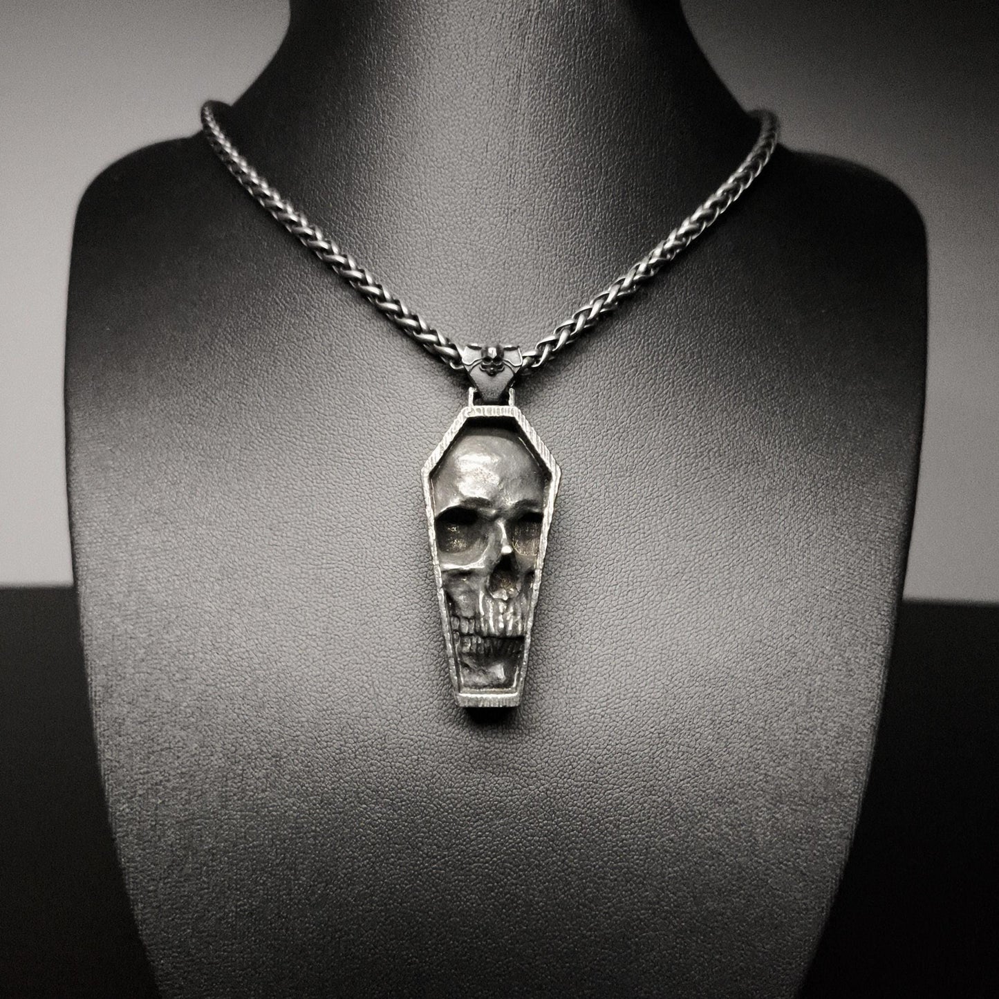 Skull-shaped pendant on a chain necklace displayed on a mannequin bust.