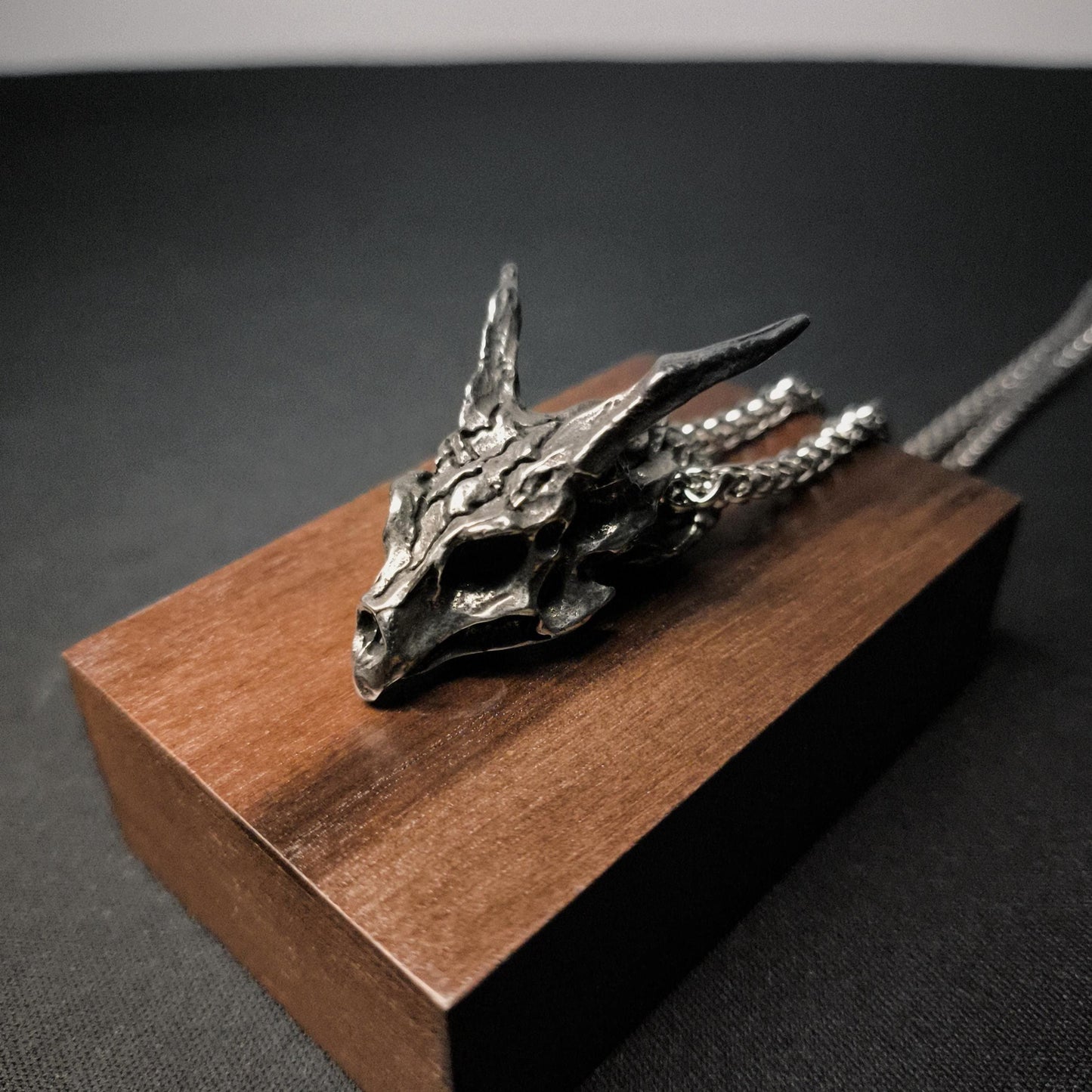 A silver dragon skull pendant chain necklace displayed on a wooden stand.