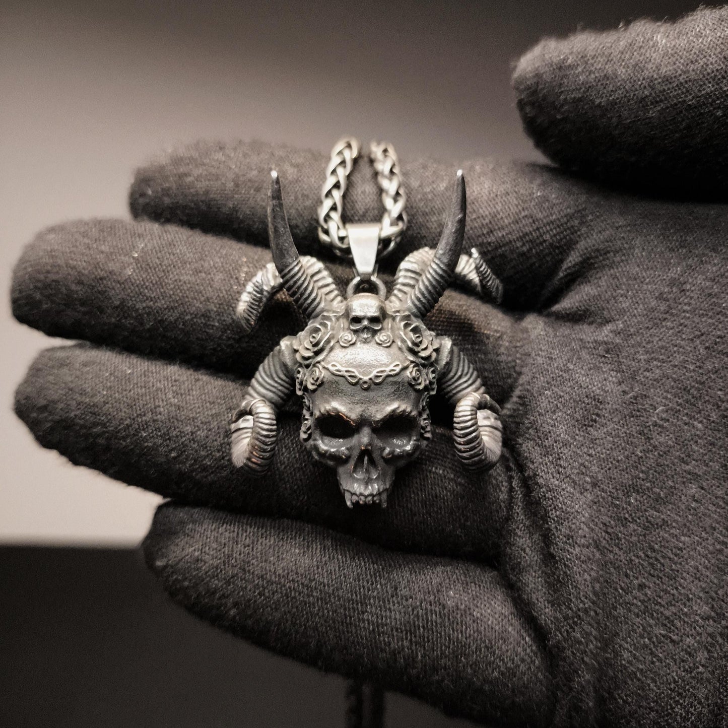 Silver pendant with skull and horns held in a gloved hand against a dark background