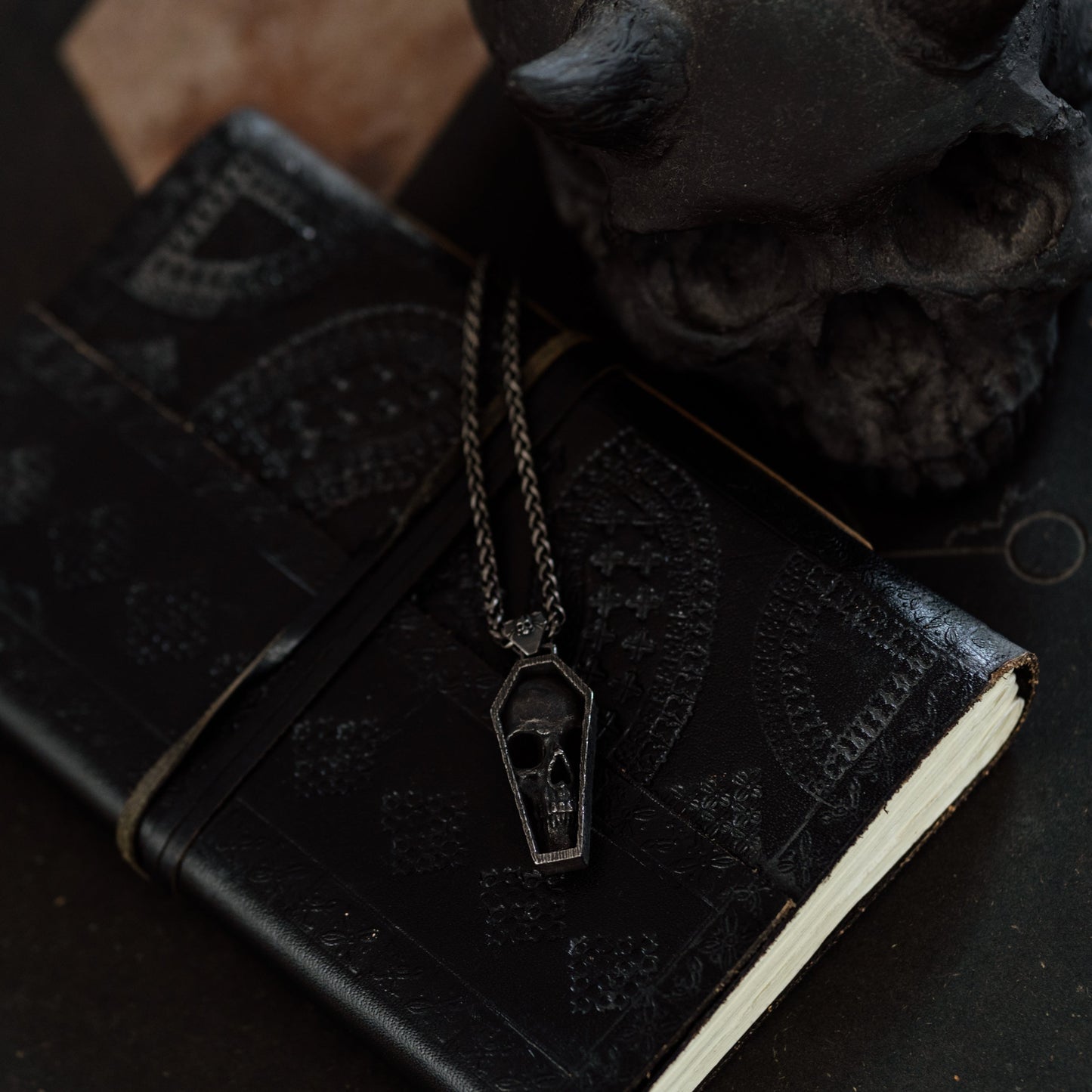 Black leather notebook with a necklace featuring a pendant on a dark surface