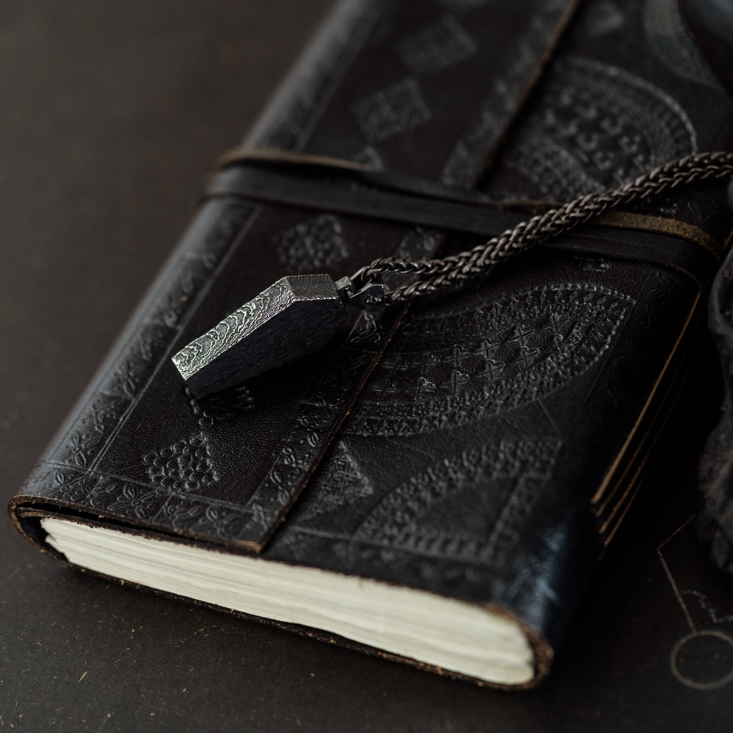 Black leather-bound notebook with chain and clasp on a dark surface