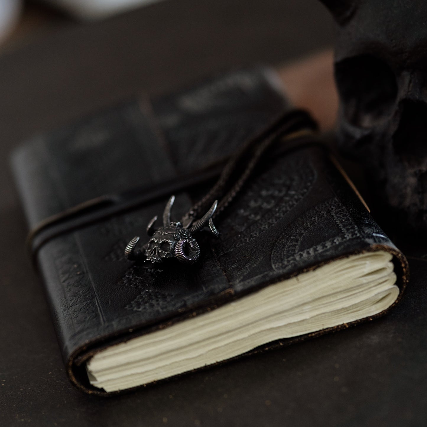 Black leather-bound notebook with a skull design on a dark surface