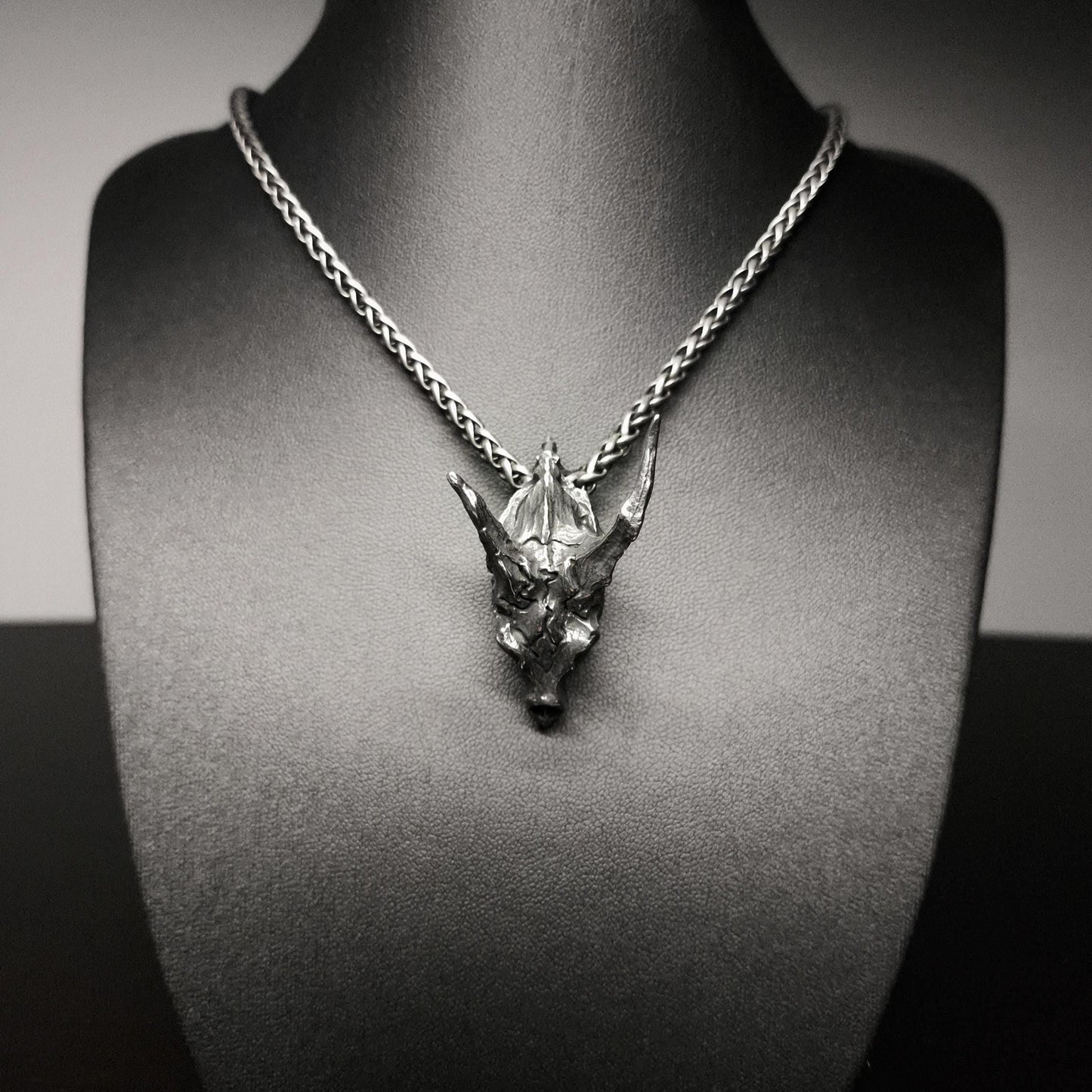 Silver necklace with a detailed pendant on a black mannequin bust.