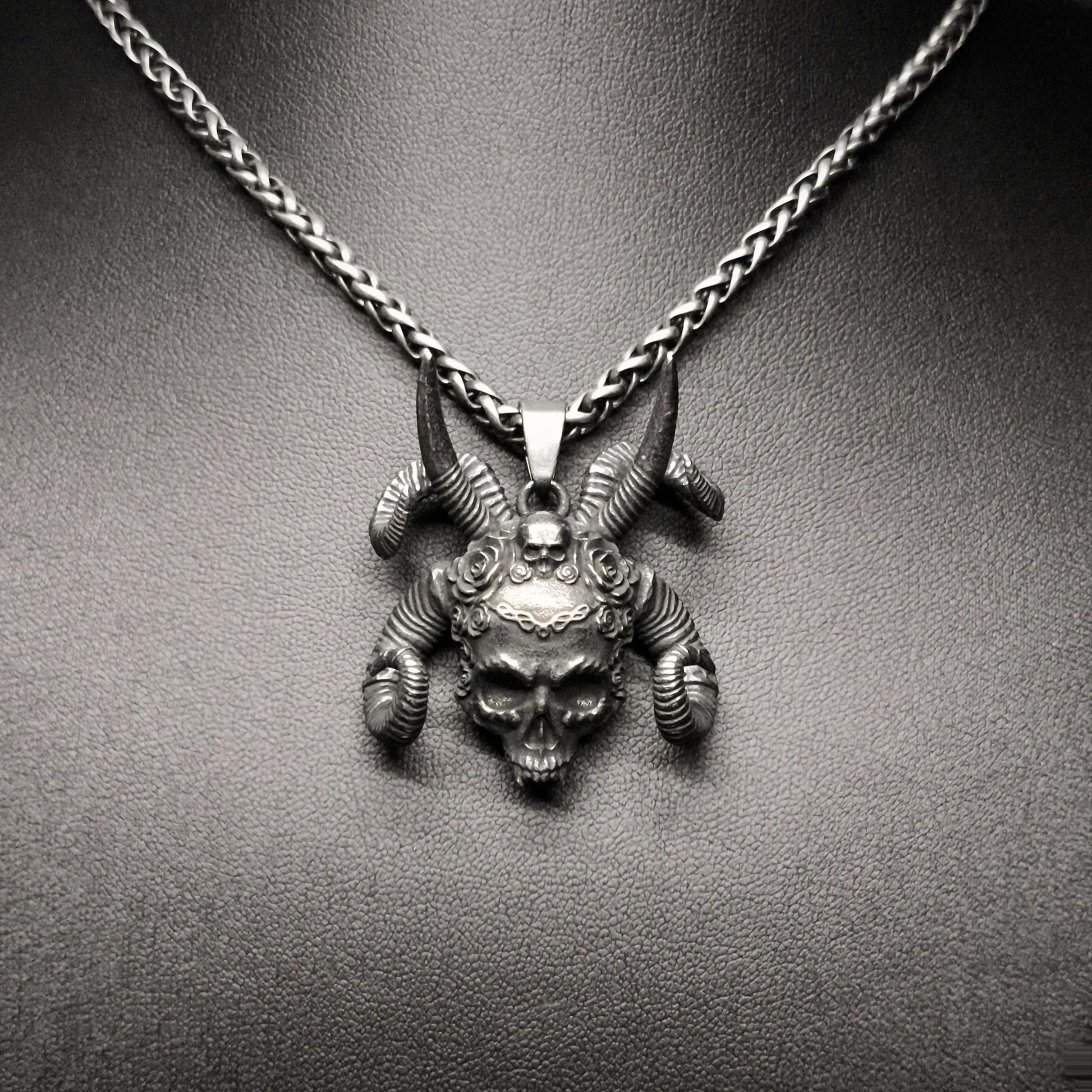 A stainless steel pendant featuring a tribal skull design, displayed on a mannequin neck.