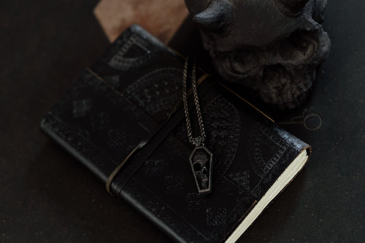 Black leather notebook with a necklace featuring a pendant on a dark surface