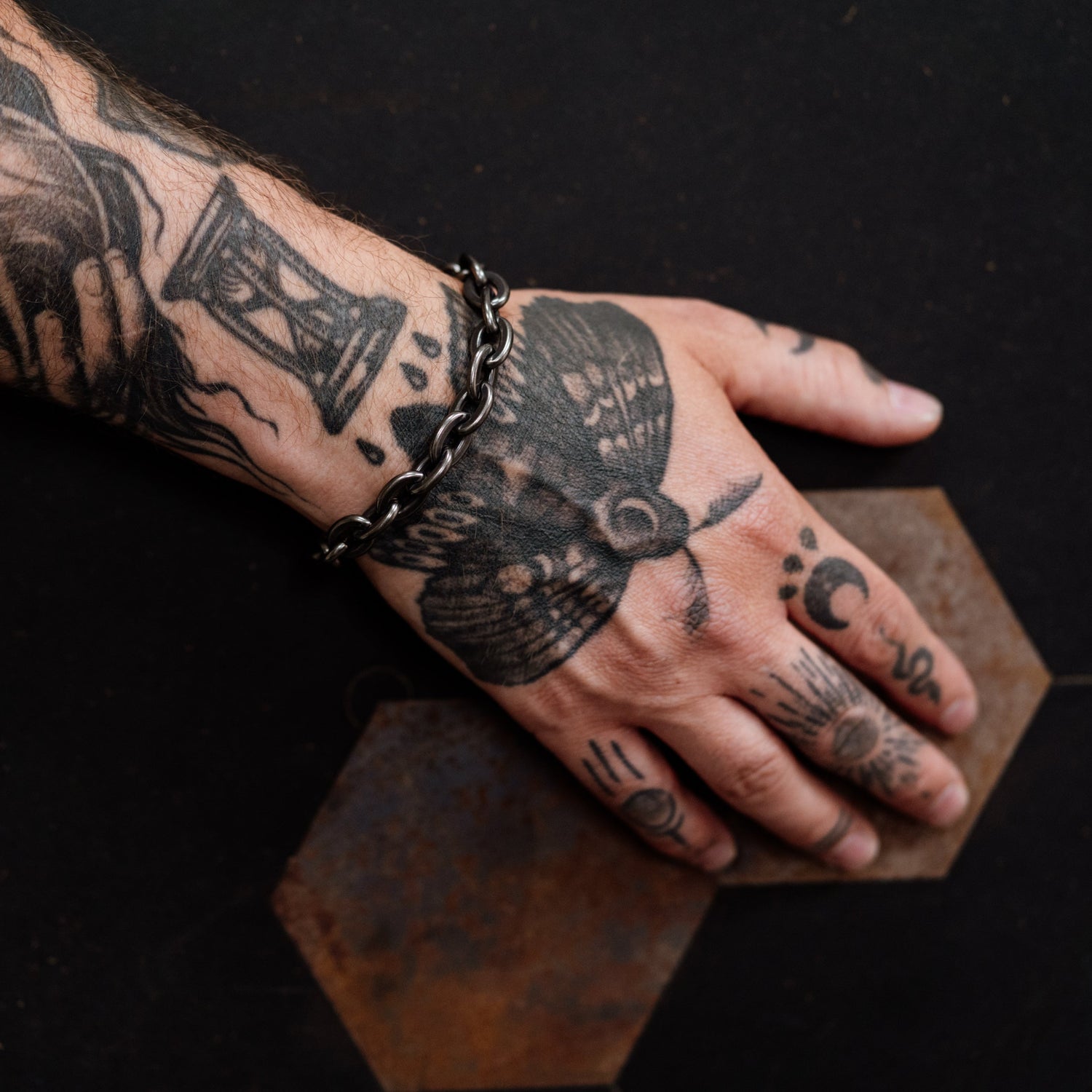 Hand with tattoos wearing a bracelet on a dark background