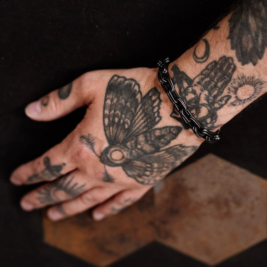 Hand with tattoos wearing a black bracelet on a dark background
